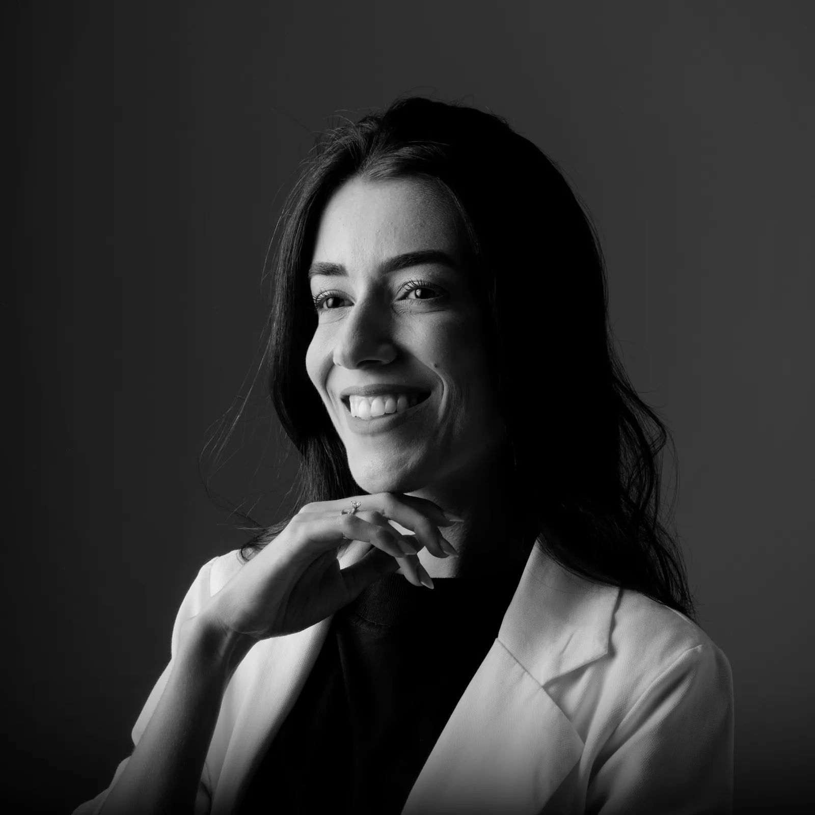 Mujer sonriendo con una sonrisa estética renovada, retrato en blanco y negro sobre fondo gris