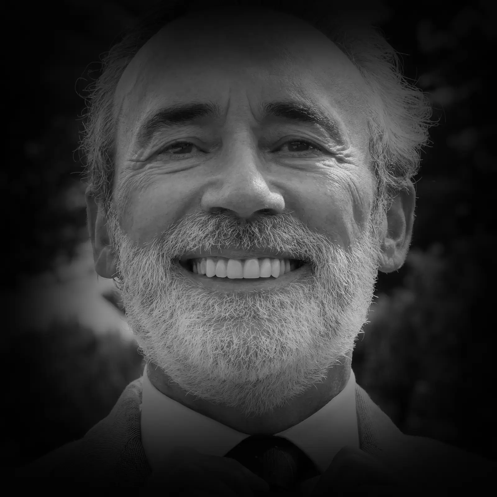 Hombre mayor sonriendo con confianza tras su tratamiento de implantes, retrato en blanco y negro sobre fondo gris