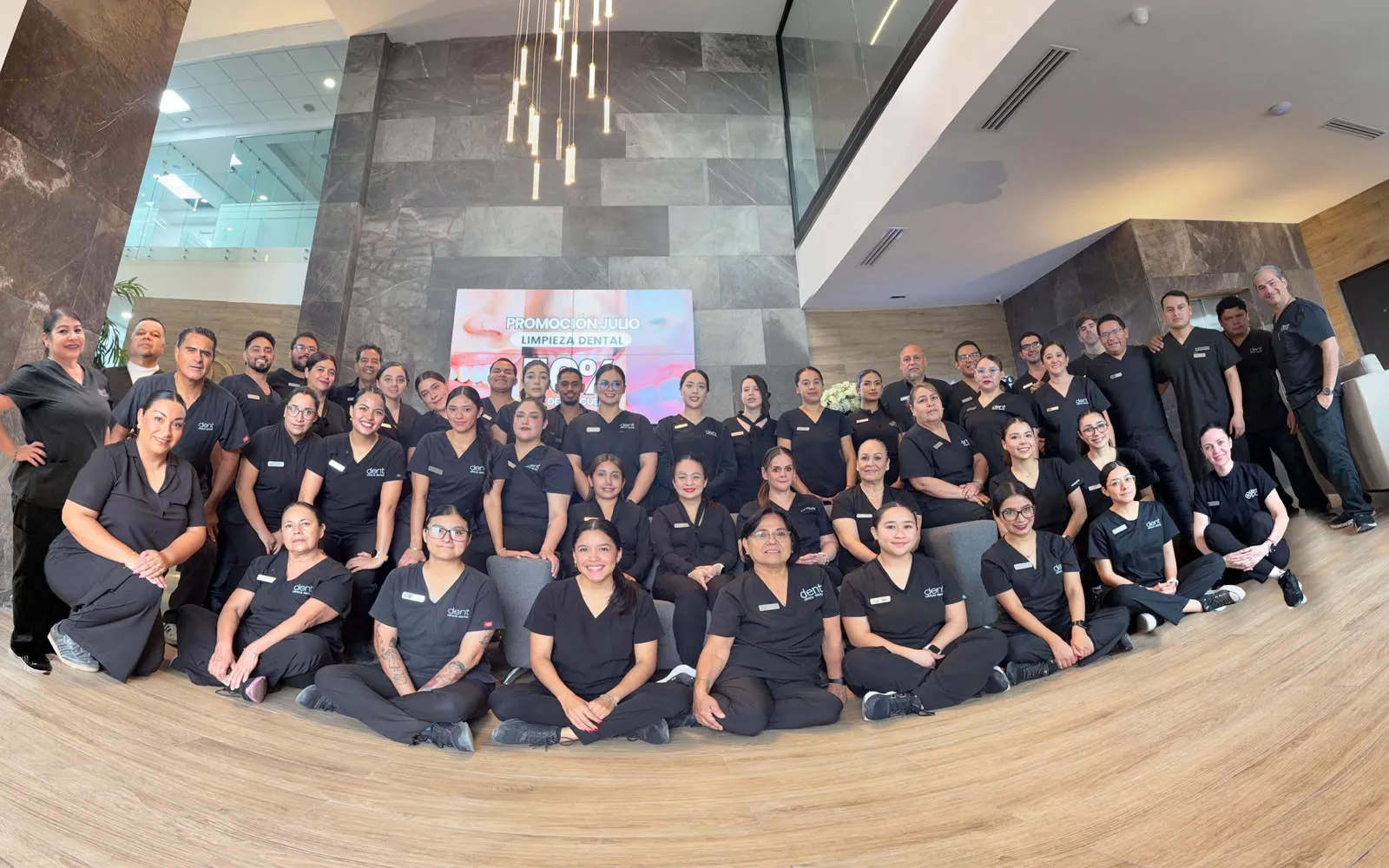 El equipo completo de Dent Clínica Dental frente al muro con el logotipo de la clínica